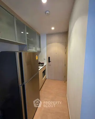 Compact modern kitchen with stainless steel fridge and built-in oven in cozy apartment.