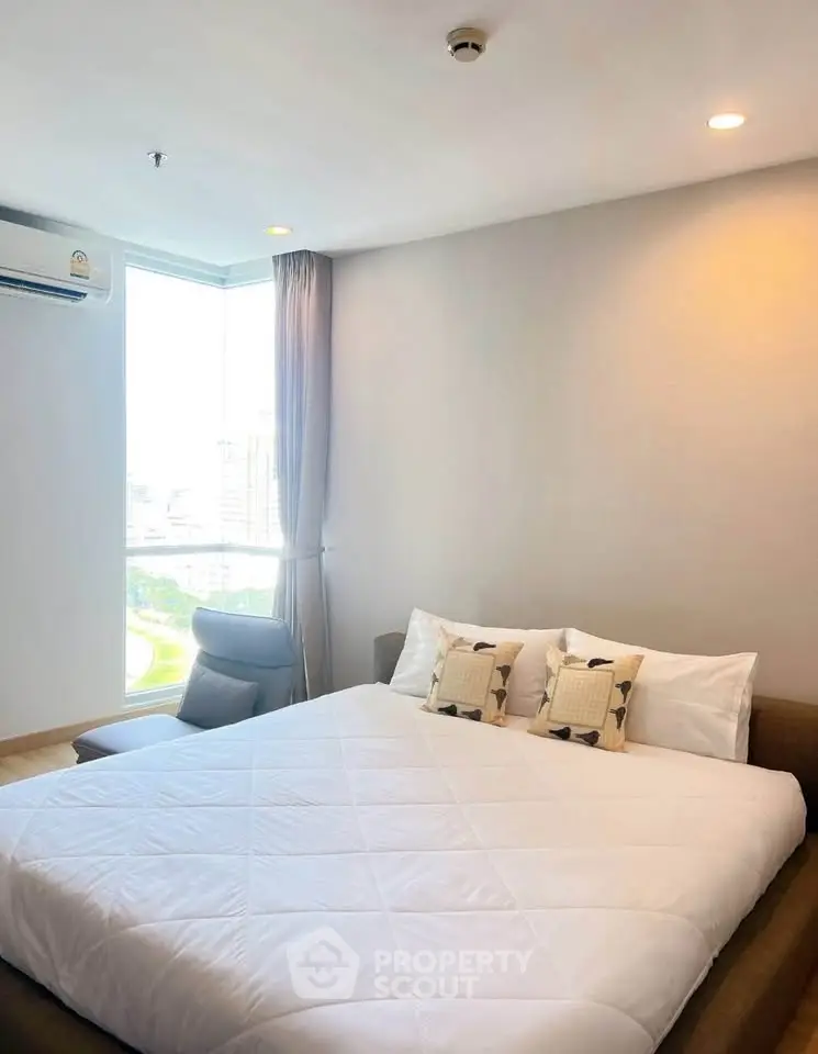 Modern bedroom with large window and city view, featuring a cozy bed and stylish decor.