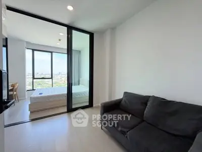 Modern apartment with glass partition, cozy sofa, and panoramic city view from bedroom.