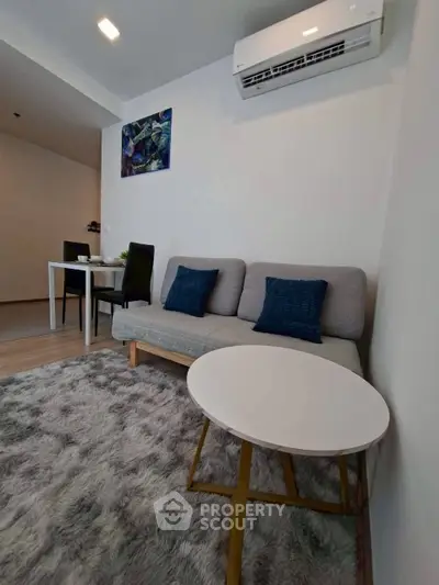 Modern living room with cozy sofa, stylish rug, and dining area in open layout apartment.
