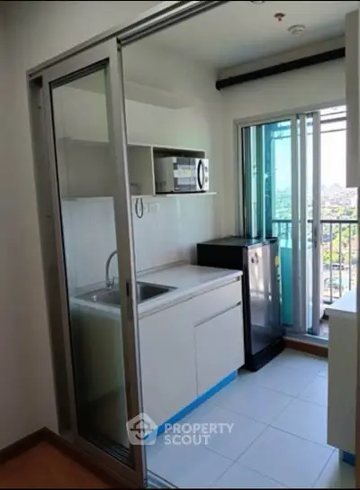 Modern compact kitchen with sliding glass door and city view, featuring microwave and fridge.