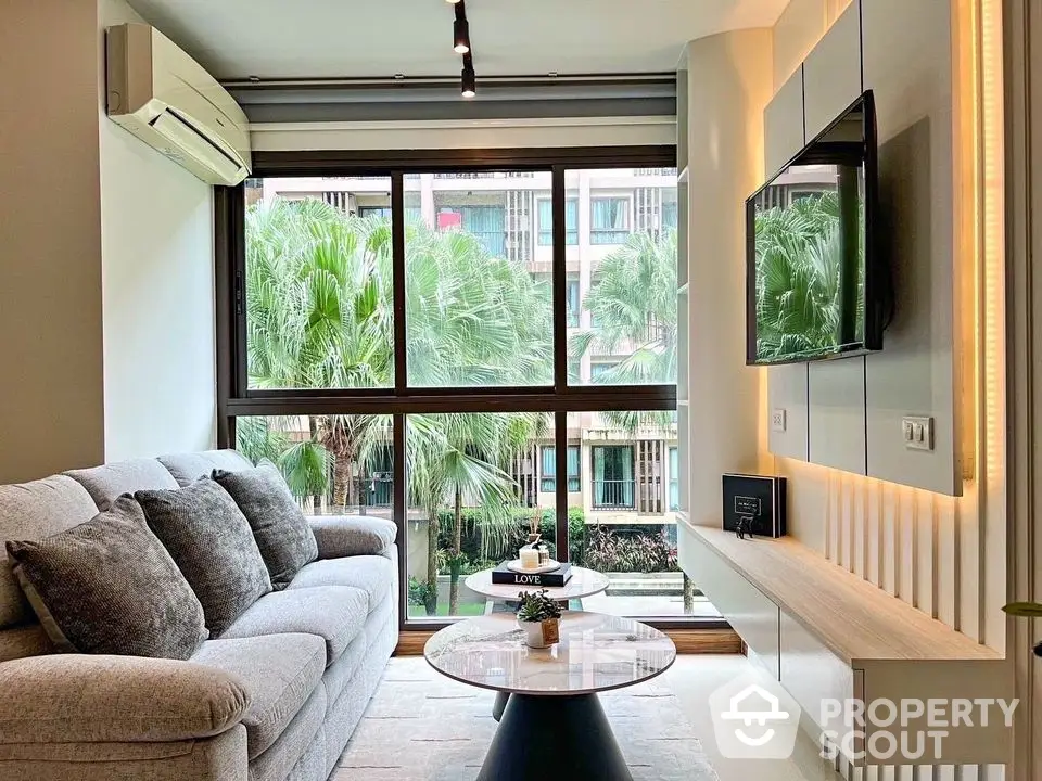 Modern living room with large windows and stylish decor overlooking lush greenery.