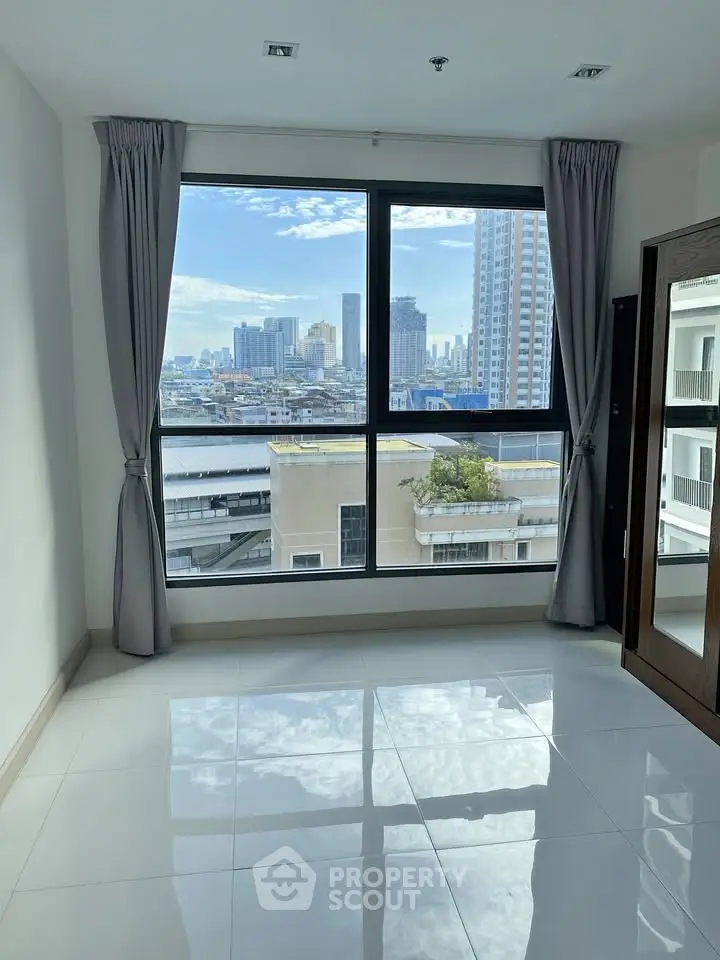 Spacious room with large window offering stunning city skyline view, perfect for urban living.