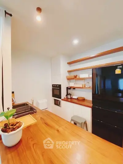 Modern kitchen with sleek black fridge and built-in oven, featuring wooden countertops and open shelving.