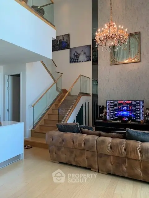 Luxurious living room with high ceiling, elegant chandelier, and stylish staircase in modern home.