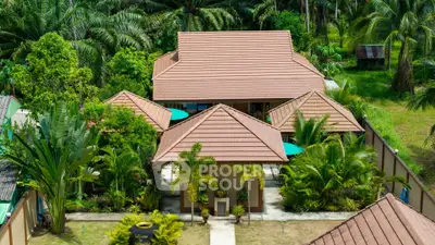 Tropical villa surrounded by lush greenery, featuring multiple peaked roofs and a serene garden setting.