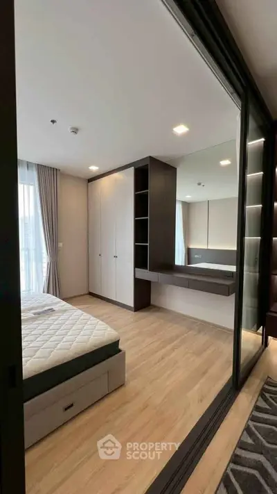 Modern bedroom with sleek design, built-in wardrobe, and large mirror reflecting natural light.