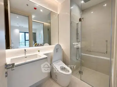 Modern bathroom with glass shower and city view from adjacent room.