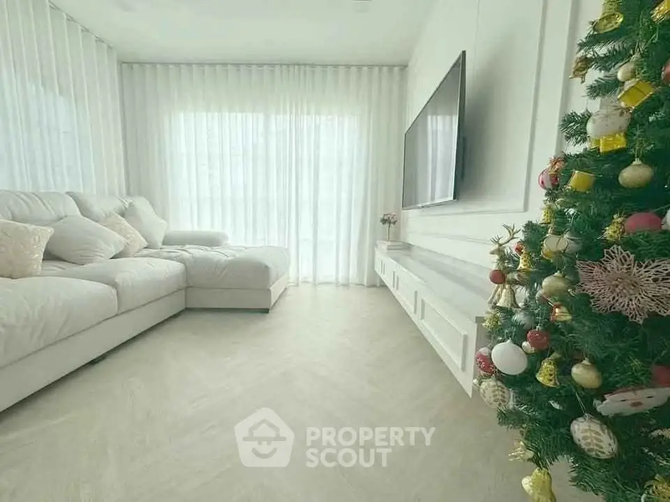 Bright living room with elegant decor and Christmas tree, featuring a cozy white sofa and large TV.
