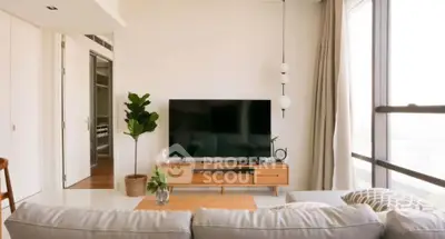 Modern living room with large TV, stylish furniture, and natural light from floor-to-ceiling windows.