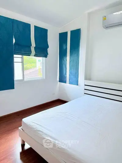 Bright bedroom with blue curtains and air conditioning, featuring a minimalist white bed frame.
