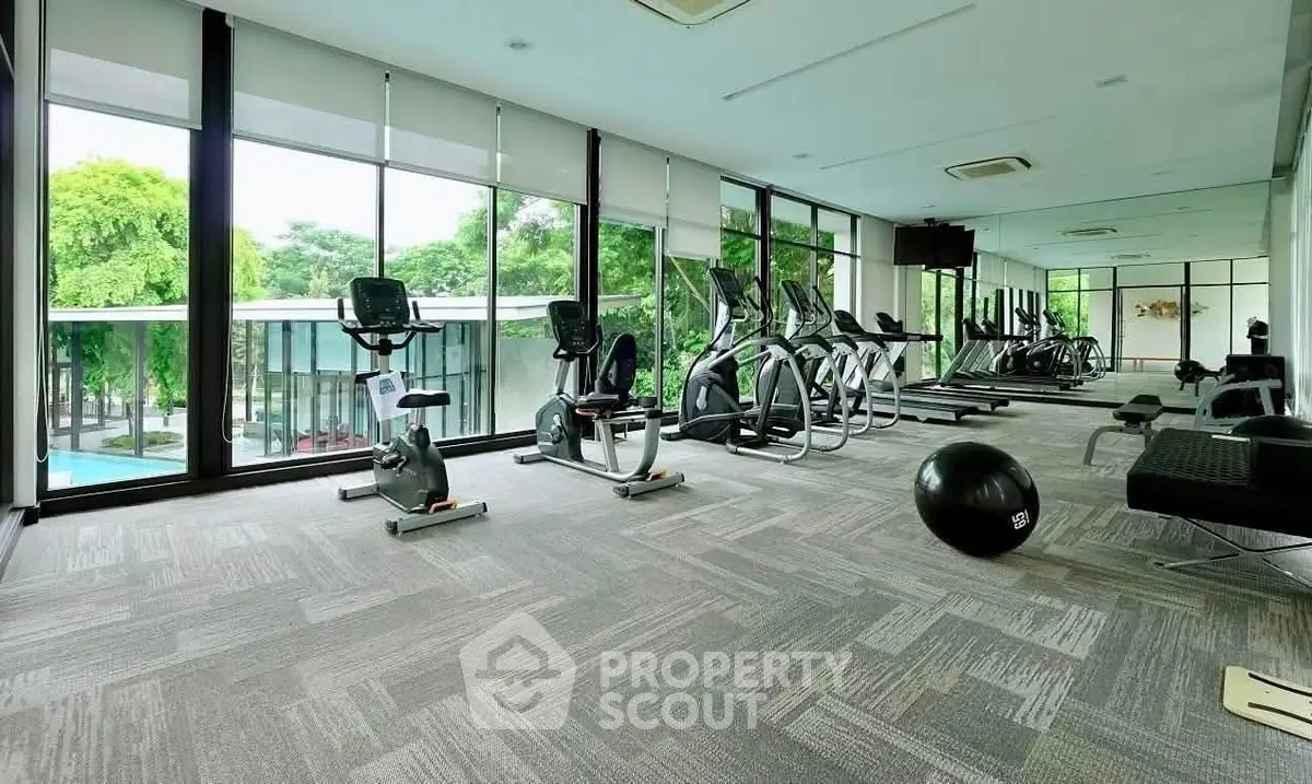 Spacious modern gym with large windows and lush greenery view, featuring state-of-the-art fitness equipment.