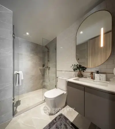 Modern bathroom with sleek design, featuring a glass shower, oval mirror, and elegant fixtures.
