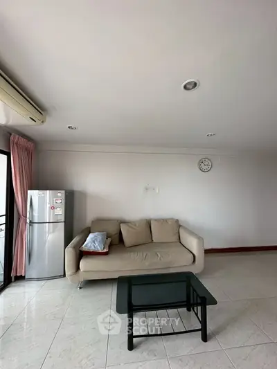 Spacious living room with modern sofa and glass coffee table, featuring a sleek refrigerator and air conditioning.