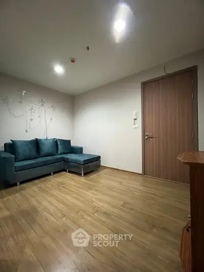 Spacious living room with modern teal sofa and wooden flooring, perfect for relaxation and entertaining.