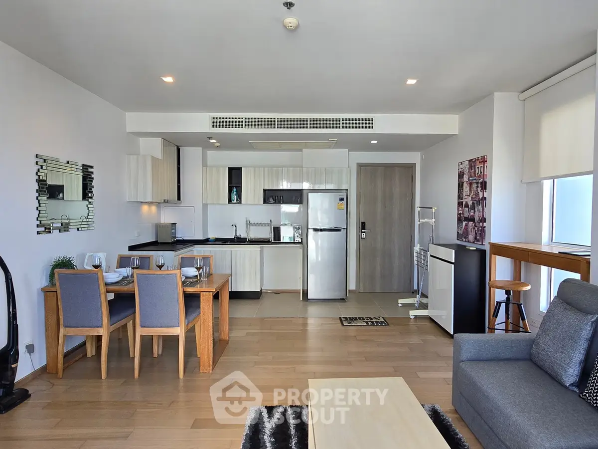 Modern open-plan living room with kitchen and dining area, featuring sleek furniture and natural light.