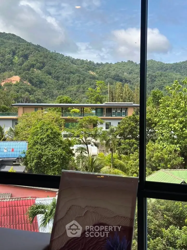 Stunning mountain view from a modern apartment window, surrounded by lush greenery and vibrant rooftops.