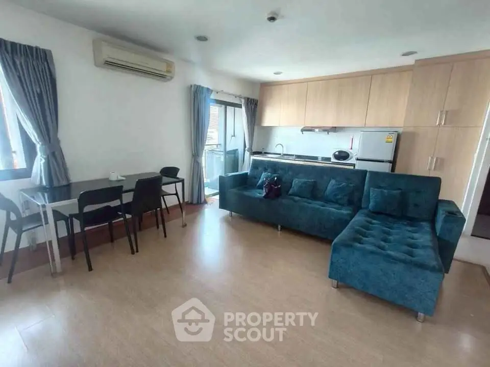 Modern living room with teal sofa and open kitchen layout, featuring sleek appliances and dining area.