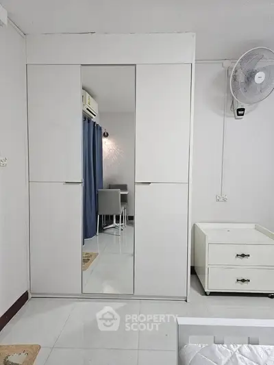 Modern bedroom with sleek wardrobe and minimalist decor, featuring a wall-mounted fan and stylish furniture.