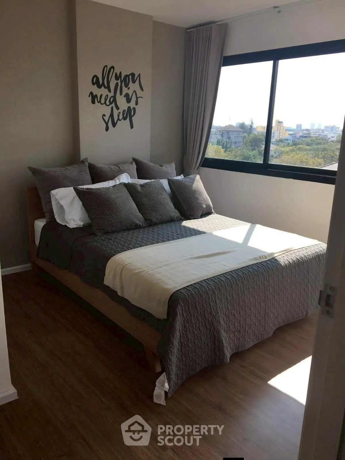 Cozy bedroom with stylish decor and large window offering natural light and city view.