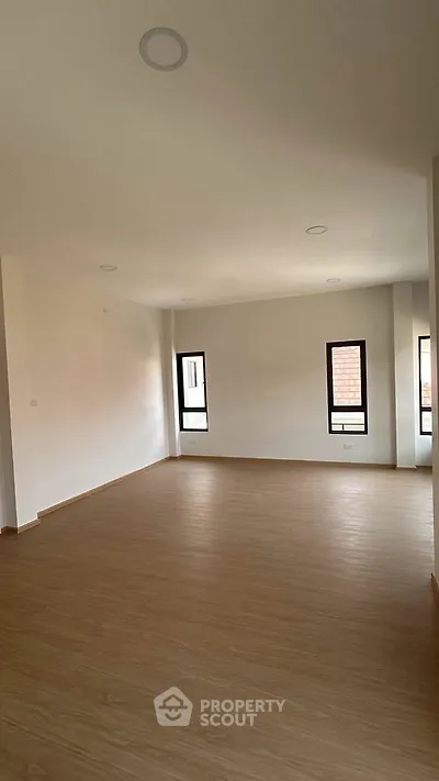 Spacious empty living room with wooden flooring and large windows for natural light.