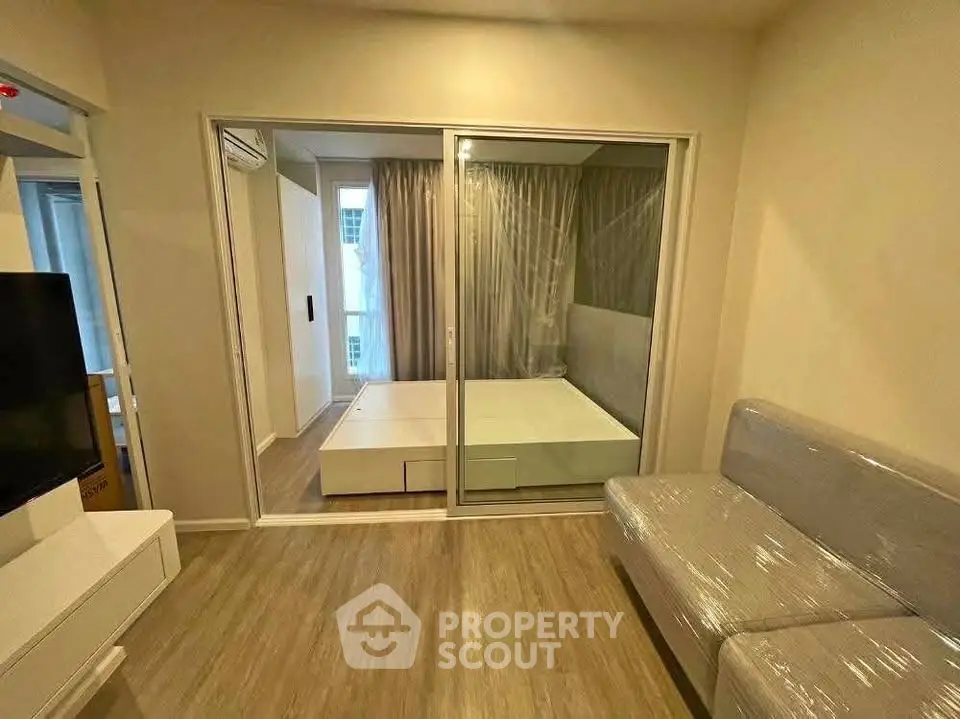 Modern living room with sliding glass doors leading to a cozy bedroom, featuring sleek furniture and wooden flooring.