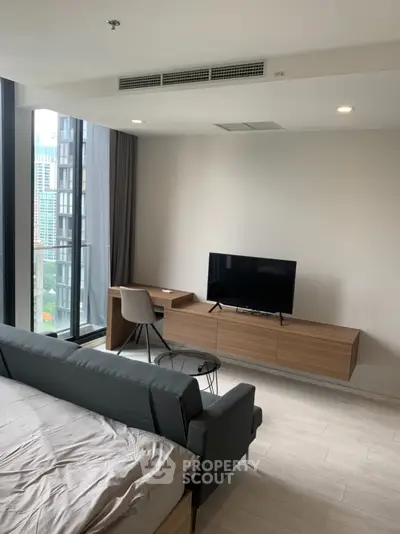 Modern studio apartment with sleek furniture and city view, featuring a cozy living area and large windows.