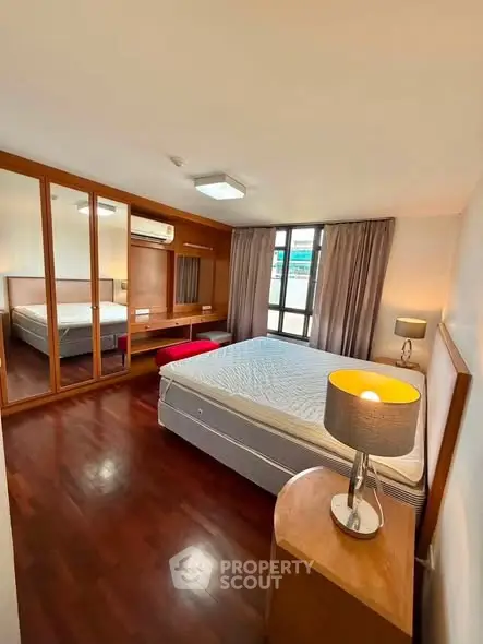 Spacious bedroom with wooden flooring and large mirrored wardrobe in modern apartment.