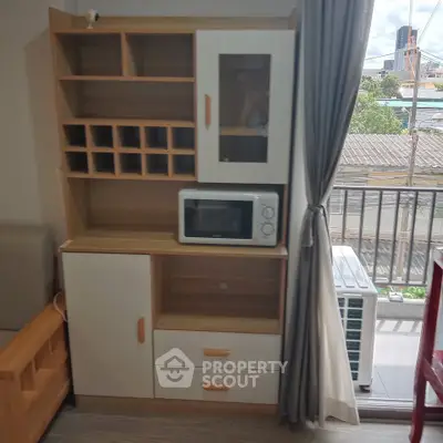 Modern apartment interior with stylish wooden cabinet and microwave near balcony view.