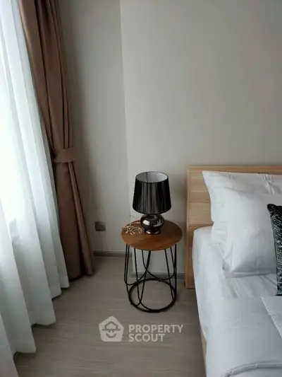 Modern bedroom with stylish bedside table and lamp, natural light through large window.