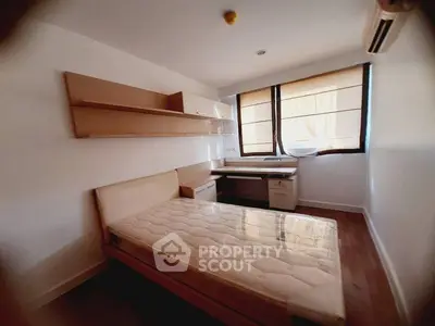 Cozy bedroom with natural light, featuring a bed, desk, and wall shelves, perfect for modern living.