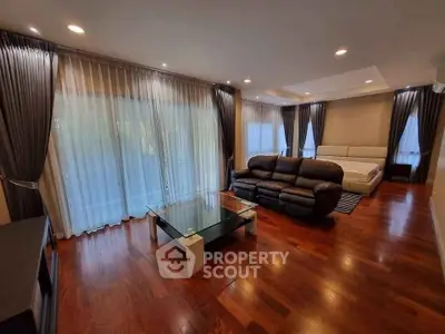 Spacious living room with elegant hardwood floors and modern furniture, featuring large windows with stylish curtains.