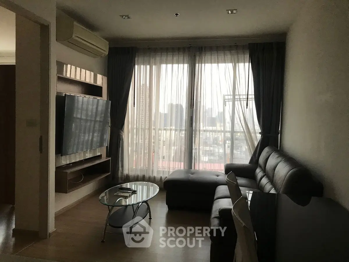 Modern living room with large TV, sectional sofa, and city view through sheer curtains.