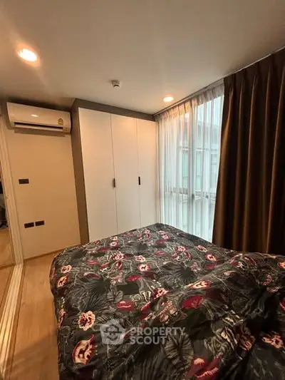 Cozy bedroom with floral bedding and ample natural light from large windows.