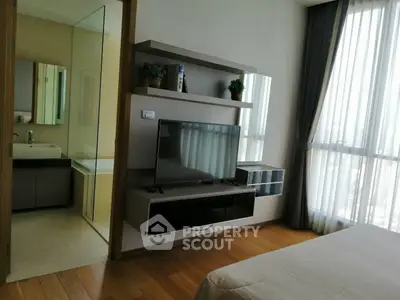 Modern bedroom with TV and bathroom view, featuring sleek wooden flooring and large windows with curtains.