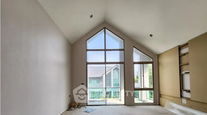 Spacious modern living room with large windows and high ceiling, offering a bright and airy atmosphere.