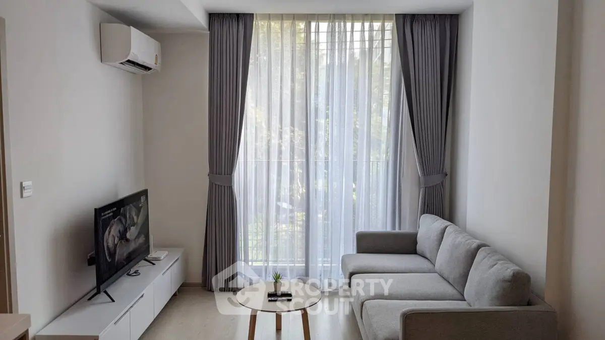 Modern living room with sleek gray sofa, flat-screen TV, and large window with elegant curtains.