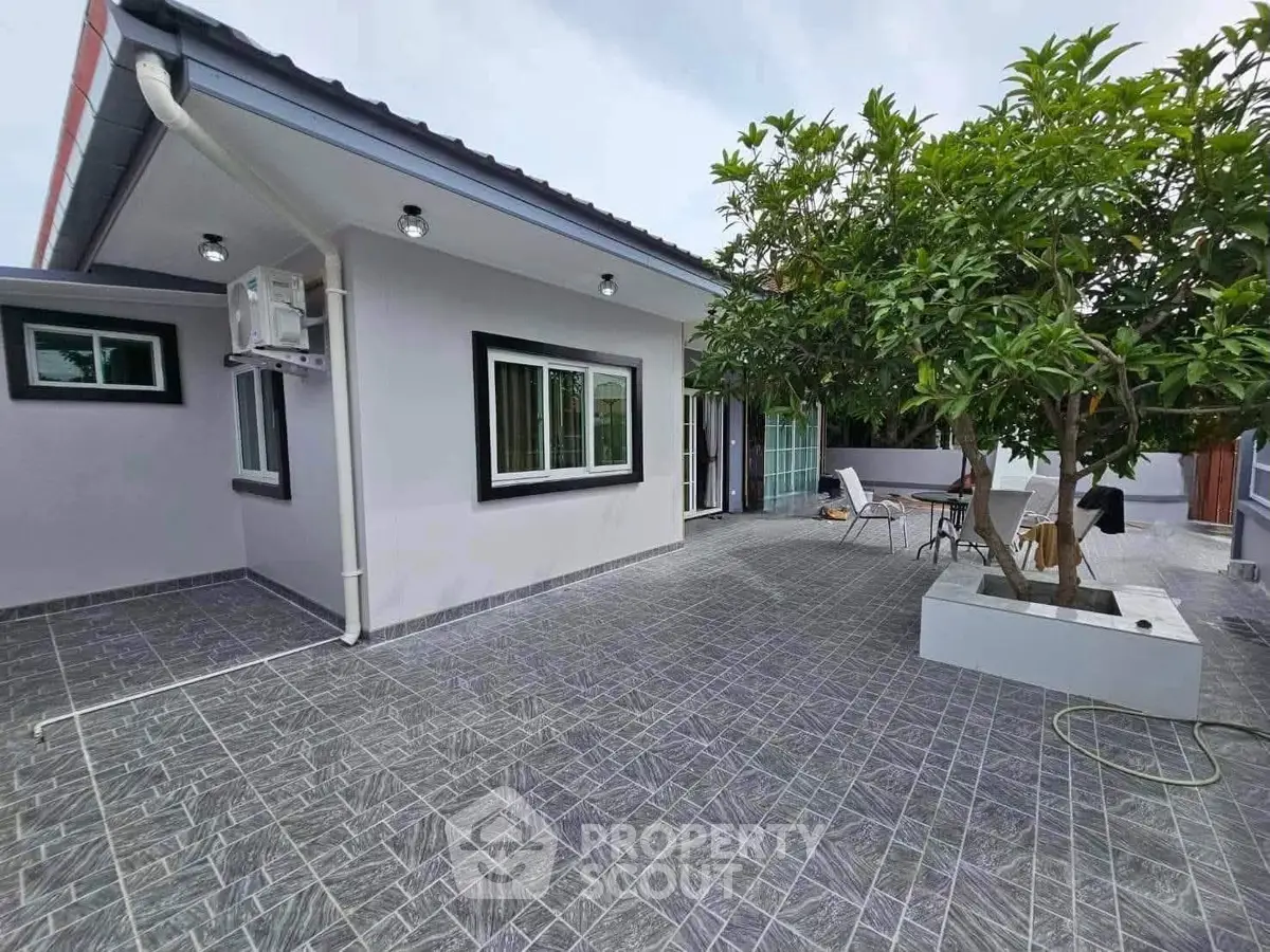 Charming single-story home with spacious tiled patio and lush greenery, perfect for outdoor relaxation.