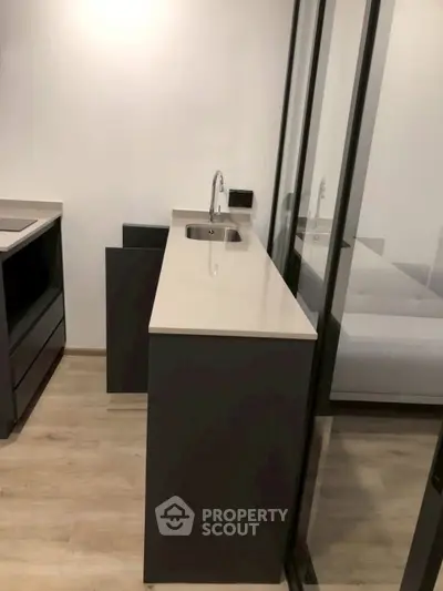 Modern kitchen with sleek design and glass partition, featuring minimalist cabinetry and a compact sink.