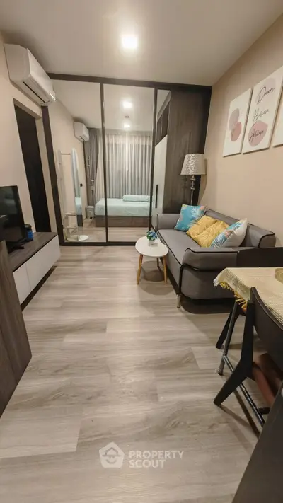 Modern living room with cozy sofa and stylish decor leading to a bedroom through glass doors.