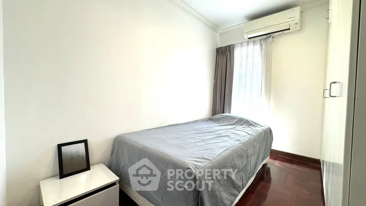Cozy bedroom with air conditioning and natural light, featuring a minimalist design and wooden flooring.
