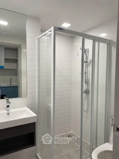 Modern bathroom with glass shower enclosure and sleek vanity in contemporary apartment.