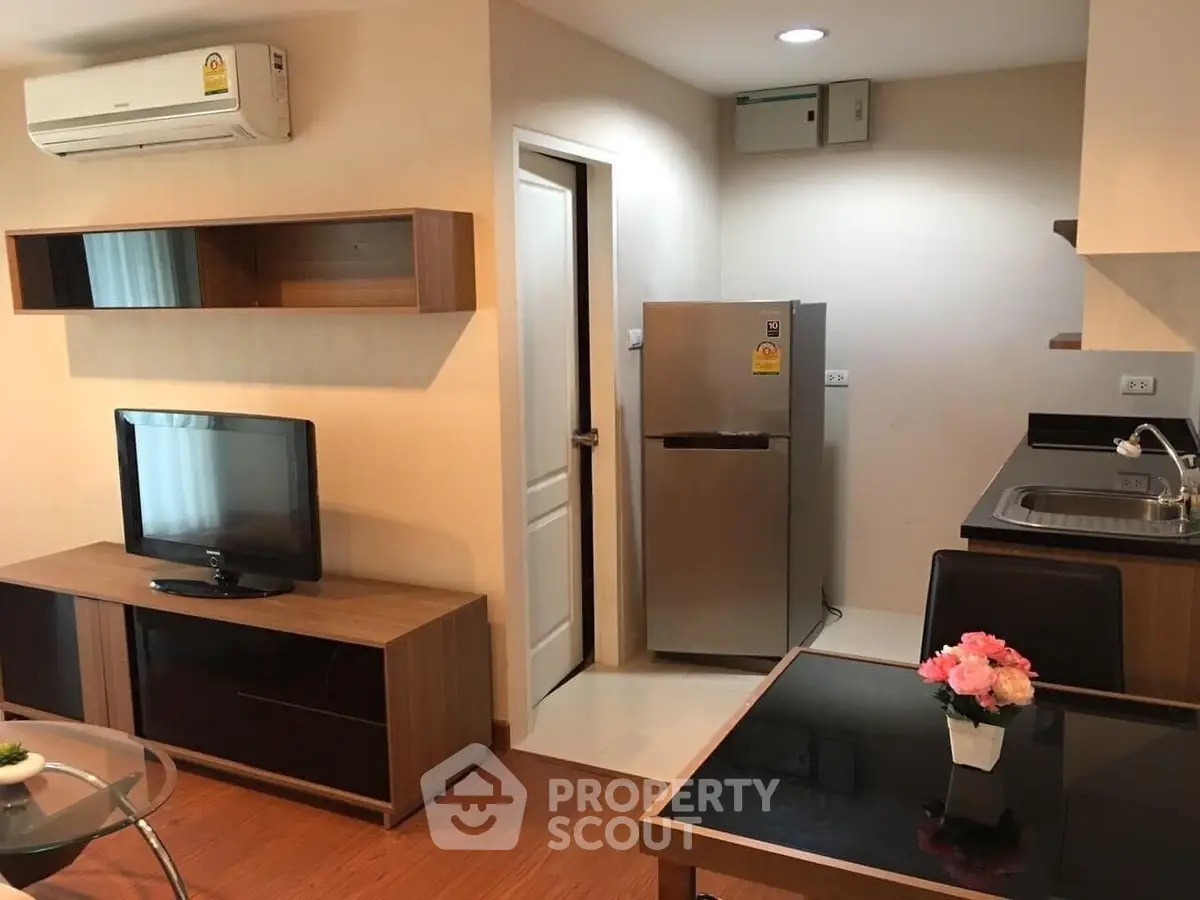 Modern apartment interior with cozy living room and compact kitchen featuring stainless steel fridge and sleek design.