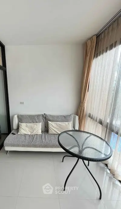 Modern living room with sleek sofa and glass table, featuring floor-to-ceiling windows and elegant curtains.