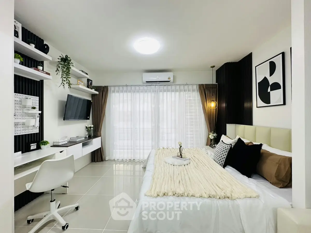 Modern bedroom with stylish decor, large window, and workspace area, perfect for urban living.