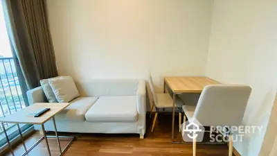 Cozy and modern living space featuring a comfortable white sofa, wooden dining table with chairs, and natural light streaming in from the balcony door.