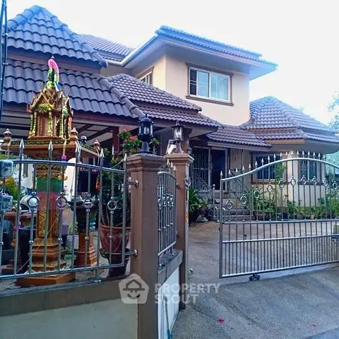 Charming two-story house with tiled roof and gated entrance, featuring a decorative spirit house in the garden.