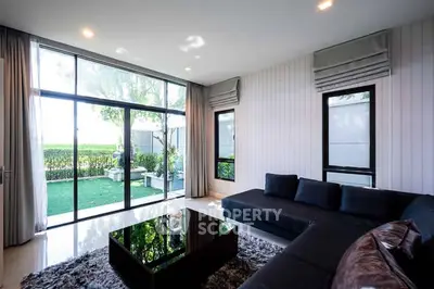 Modern living room with large windows and garden view, featuring sleek black furniture.