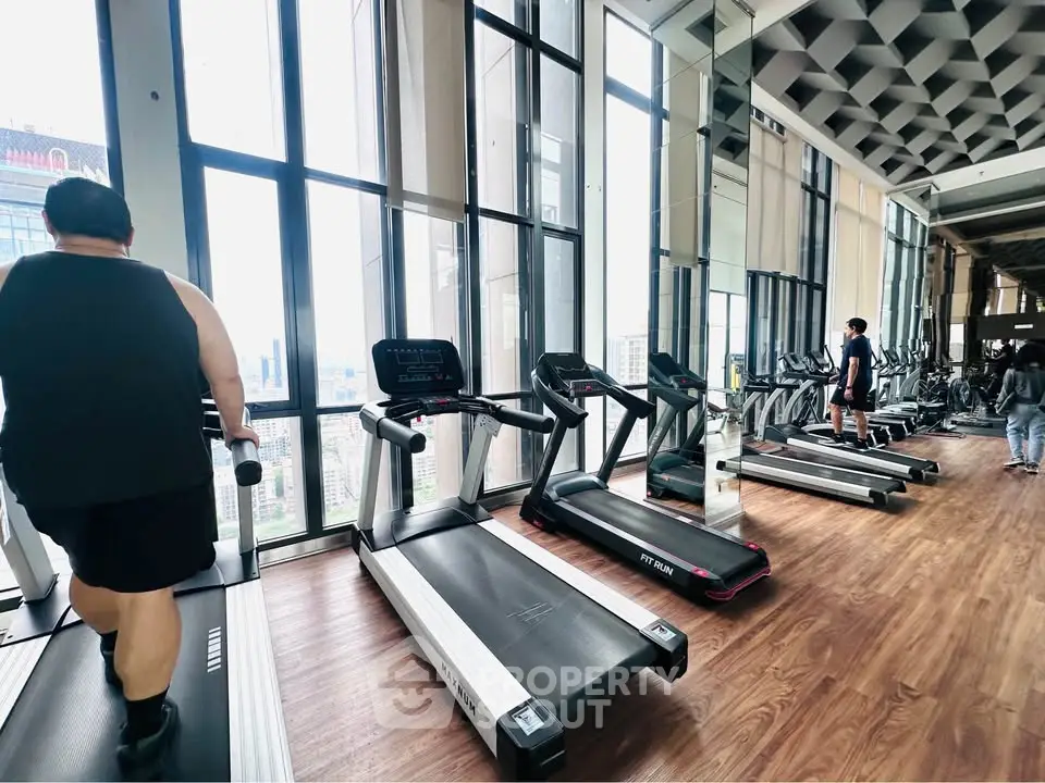 Spacious gym with modern equipment and city view, perfect for fitness enthusiasts.