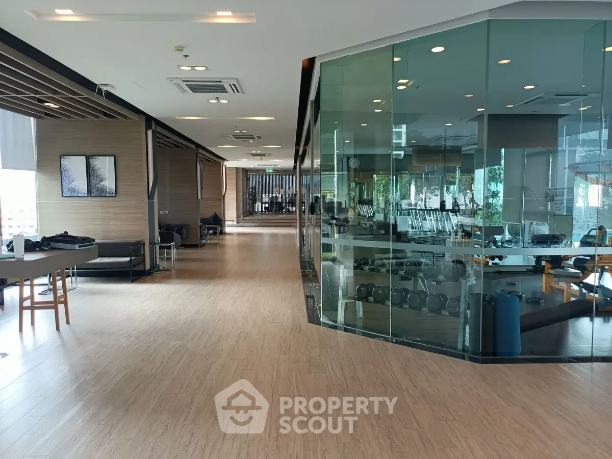 Spacious modern gym with glass walls and wooden flooring in luxury building.